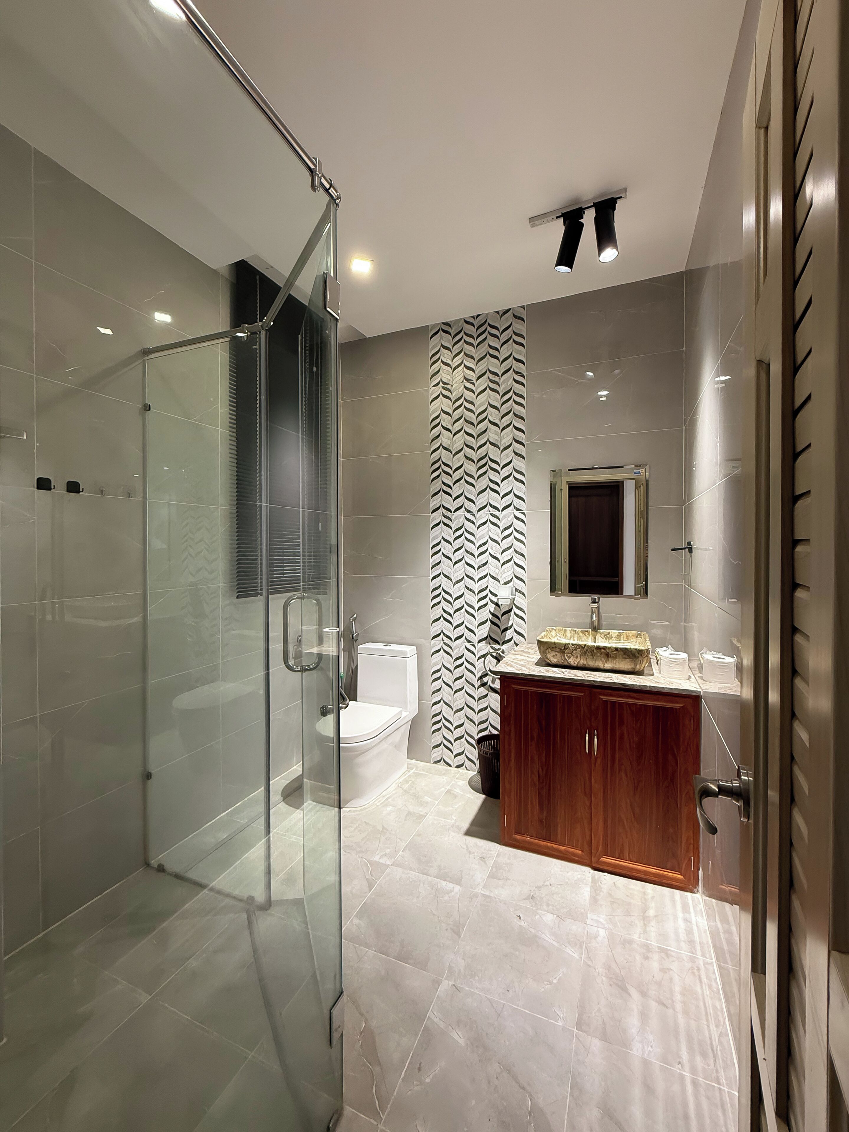 A modern bathroom with a glass-enclosed shower, a toilet, and a vanity with a marble countertop.