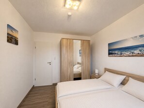 A bedroom with a bed, a nightstand, a mirror, and a painting on the wall. - Family-friendly bungalow near the Kurpark in Norddeich—close to the beach, with a garden, and dog-friendly (Norden)