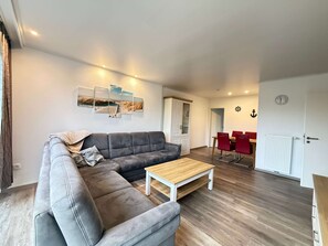 En moderne stue med en hjørnesofa, et træsofabord og et spiseområde med røde stole.