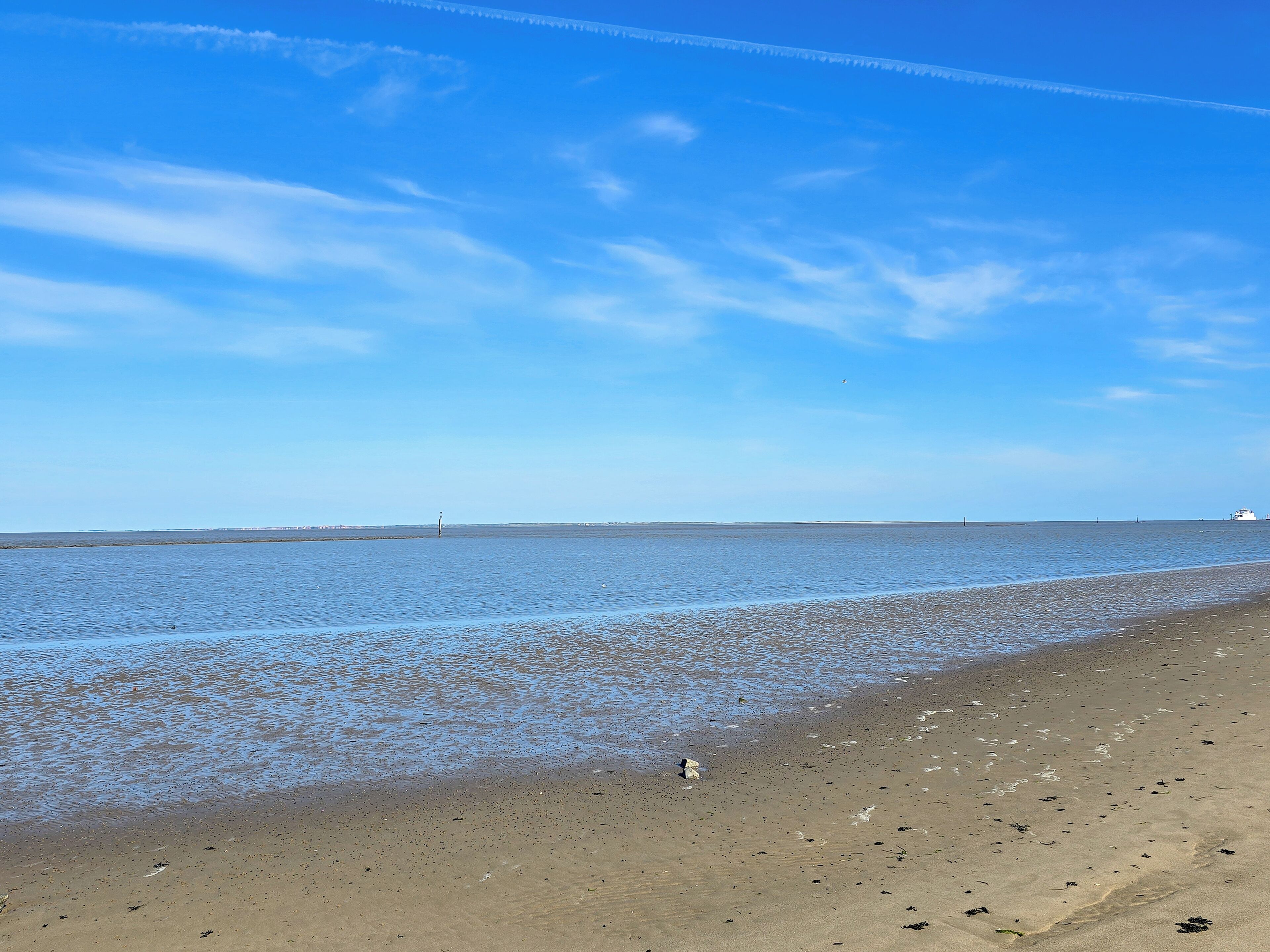 Une plage avec un ciel dégagé, une eau calme et un phare situé au loin.