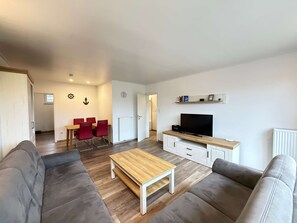 A modern living room with a sofa, a coffee table, a TV, and a dining area with chairs. - Family-friendly bungalow near the Kurpark in Norddeich—close to the beach, with a garden, and dog-friendly (Norden)