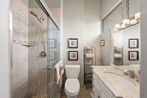 Ein modernes Badezimmer mit einer gläsernen Duschkabine, einer weißen Toilette, einem Marmorwaschbecken und gerahmten Bildern an den Wänden.