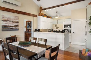 Ein Essbereich mit Holztisch und -stühlen, eine Küche mit weißen Schränken und Geräten sowie ein Deckenventilator.