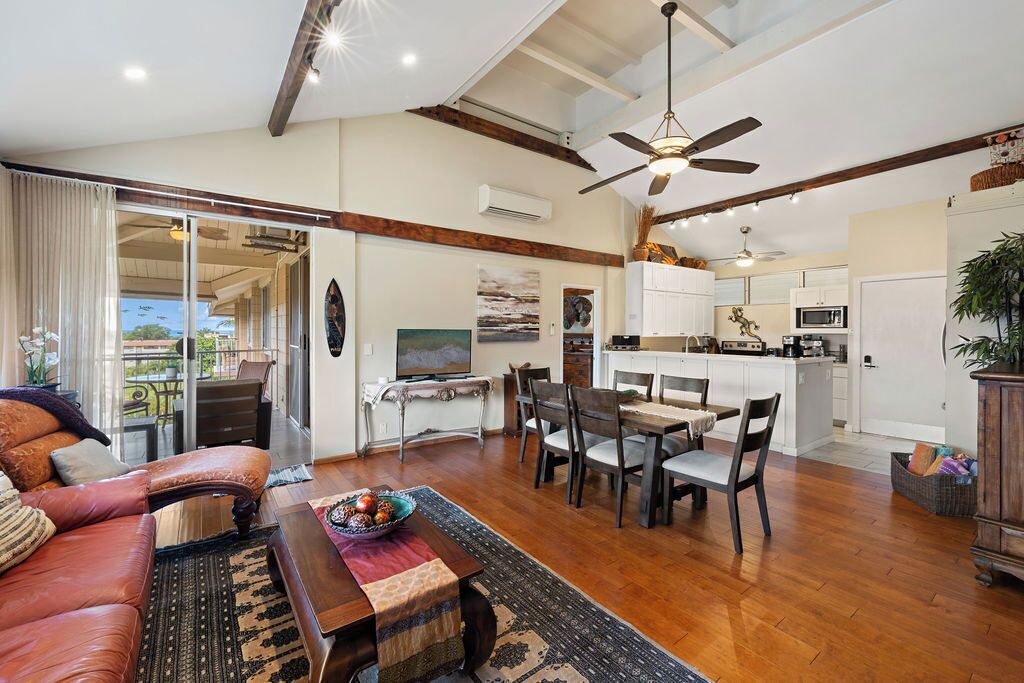 A spacious living area with a sofa, dining table, and chairs, a kitchen in the background, and a ceiling fan.