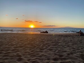A beach with a sunset, waves, and a person sitting on the sand. - Elegant top-floor unit with central AC; Haleakala Shores, steps from Kam 3 beach (Kihei)