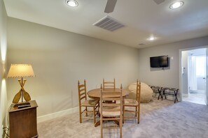 Una habitación con una mesa redonda de madera, cuatro sillas, un televisor montado en la pared y una puerta que da al baño.