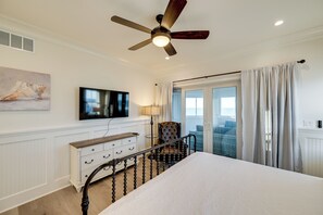 Ein Schlafzimmer mit Bett, Deckenventilator, Fernseher, Kommode, Sessel und Blick ins Freie.