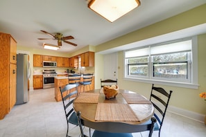 A modern kitchen with wooden cabinets, a central island, and a dining area with a round table and chairs. - Peaceful Joliet Retreat Near Dtwn & Route 66 (Joliet)