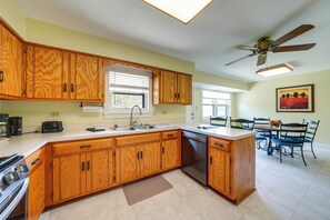 A kitchen with wooden cabinets, a built-in dishwasher, and a dining area with a table and chairs. - Peaceful Joliet Retreat Near Dtwn & Route 66 (Joliet)