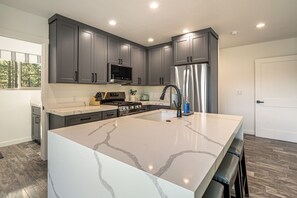 A modern kitchen with grey cabinets, a stainless steel refrigerator, a built-in microwave, and a marble island. - Mtn-Views! Flagstaff Extended Escape Near Hiking (Flagstaff)