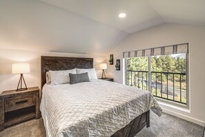 Ein Schlafzimmer mit einem großen Bett, zwei Nachttischen, einem Fenster mit Ausblick und einer Deckenleuchte.