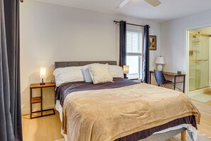Un dormitorio con cama, mesitas de noche, escritorio, silla, ventana con cortinas y zona de ducha.