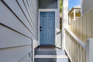 Una escalera estrecha que conduce a una puerta azul con cerradura electrónica, flanqueada por barandas blancas y revestimiento.