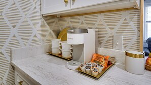 Una cocina con cafetera, tazas y alimentos envasados sobre la encimera.