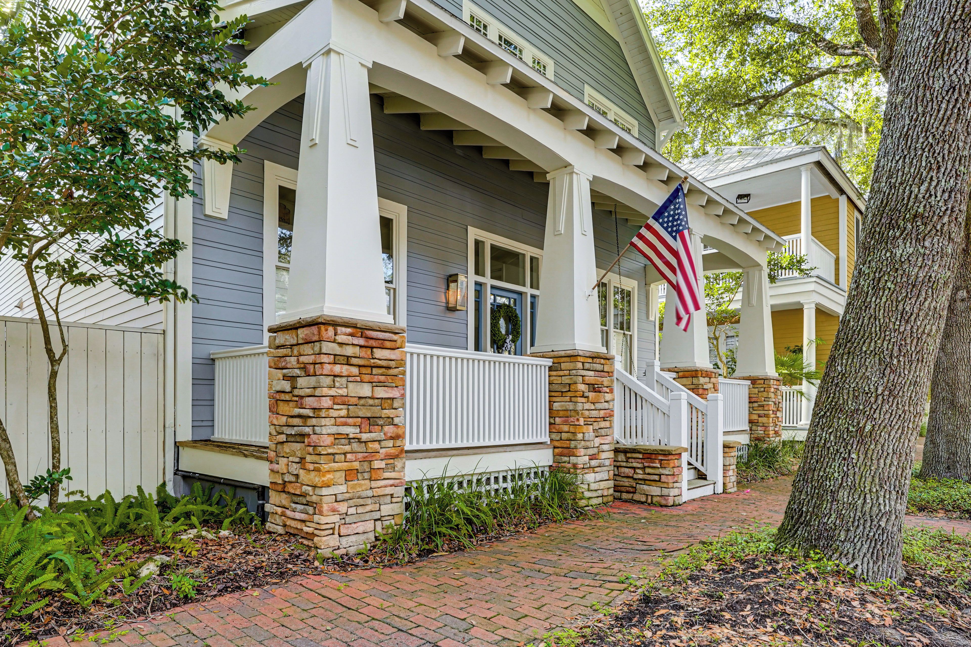 A two-story house with a porch, stone pillars, and an American flag.