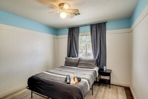 Een slaapkamer met een bed, nachtkastje, plafondventilator en een raam met gordijnen.