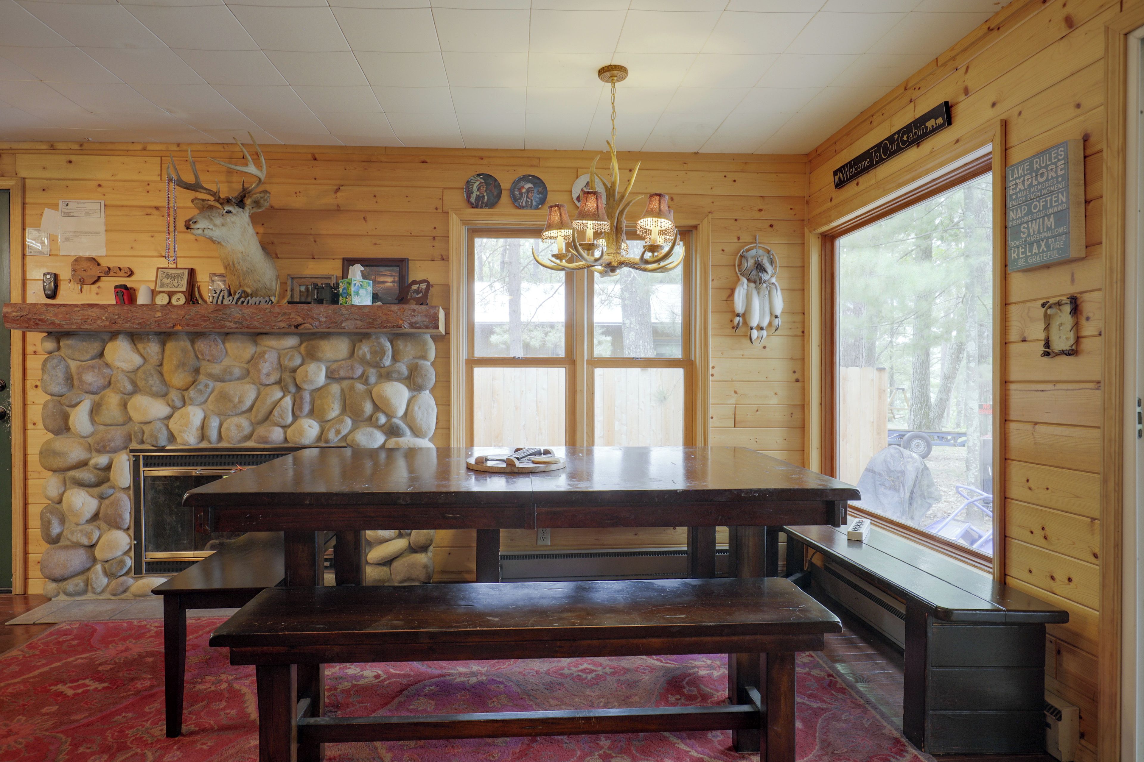 Interior de cabana com lareira de pedra, paredes de madeira, uma grande mesa de jantar e um banco.