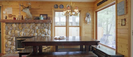 Ein Blockhaus-Interieur mit Kamin aus Stein, Holzwänden, einem großen Esstisch und einer Bank.
