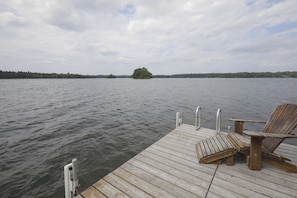 A wooden dock with a chair and a small table, overlooking a calm lake with a distant island. - Rustic & Waterside Family Cabin in Lac Du Flambeau (Lac Du Flambeau)