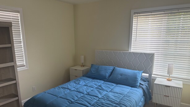 Un dormitorio con cama, mesitas de noche, cómoda y una ventana con persianas.