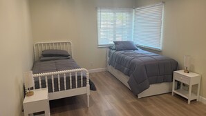 Un dormitorio con dos camas, una mesita de noche, una lámpara y una ventana con persianas.