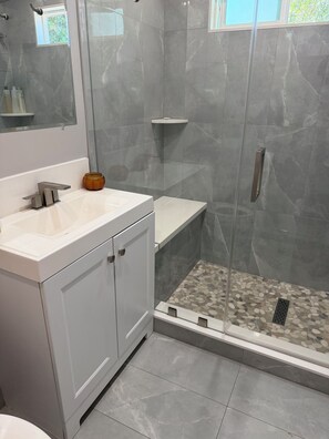 Ein modernes Badezimmer mit einer gläsernen Duschkabine, einem weißen Waschbecken und einem Marmorboden.