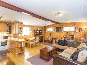 Ein gemütliches Wohnzimmer mit Holzboden, einer Couch, einem Couchtisch und einer Küchenzeile mit Holzausbau und Herd.