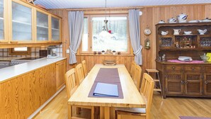 A wooden dining area with a table, chairs, and a kitchen with wooden cabinets and a window. - Hakojärventie 3b by Interhome (Kuusamo)
