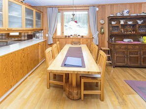 Un comedor de madera con una mesa, sillas y una cocina con armarios de madera y un ventanal.