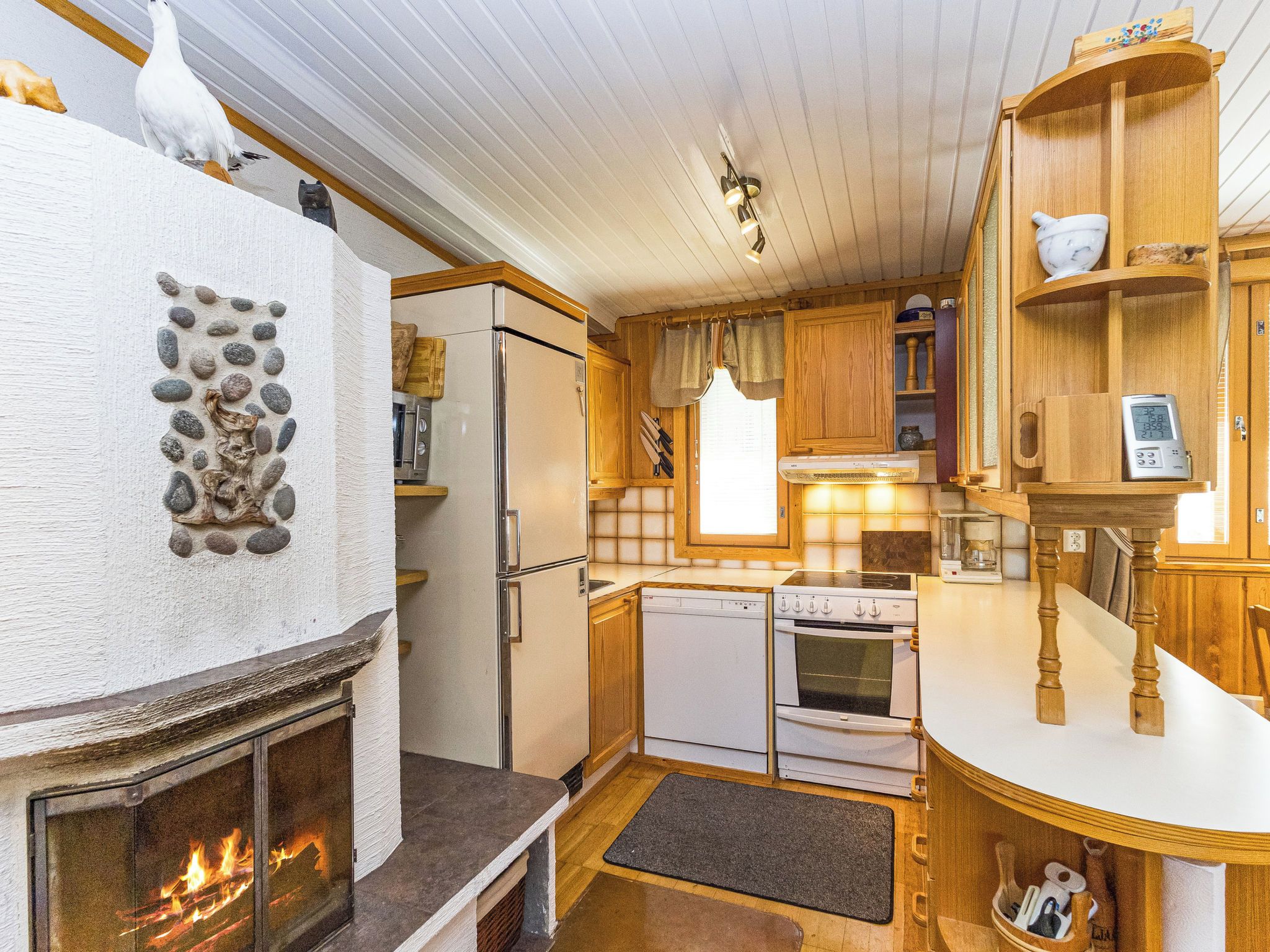 A compact kitchen with a stone wall decoration, a fireplace, a refrigerator, a dishwasher, and a stove.