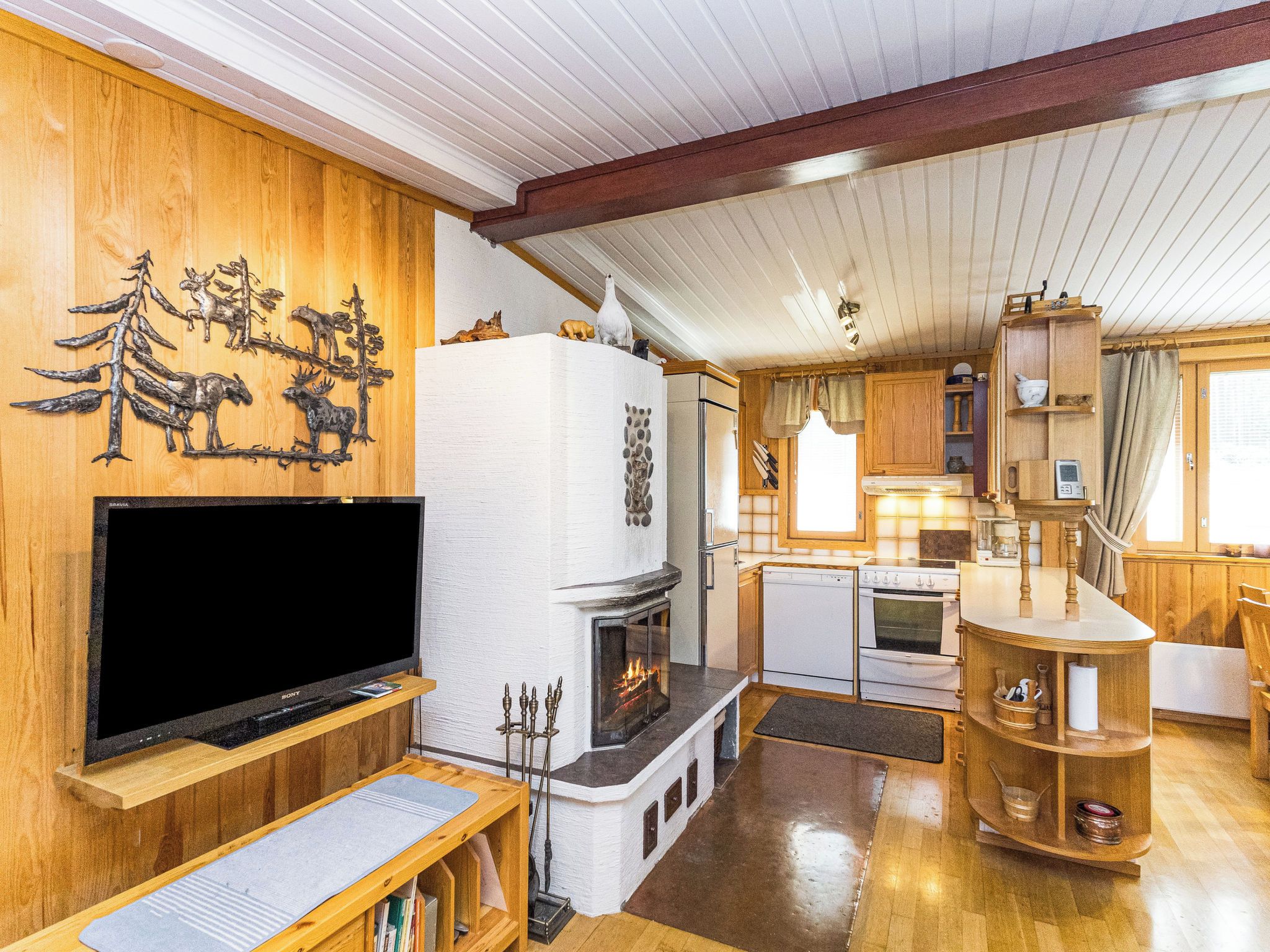 A cozy cabin interior with a fireplace, wooden walls, a television, and a kitchen area.