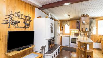 A cozy cabin interior with a fireplace, wooden walls, a television, and a kitchen area.