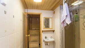 A compact bathroom with a wooden door leading to a sauna, a sink with a mirror, and a towel rack. - Hakojärventie 3b by Interhome (Kuusamo)