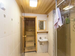 Un baño pequeño con una puerta de madera que da a una sauna, un lavamanos con espejo y un perchero para toallas.