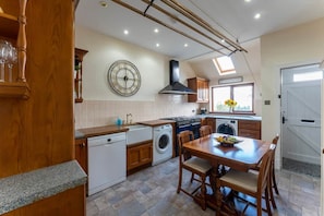 A kitchen with a dining area, wooden cabinets, a clock, and a window with a view. - St Michael's: Ben Ledi Views, Walk to Pubs & Explore Central Scotland (Kippen)