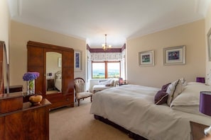 A bedroom with a large bed, a wardrobe, a chair, and a window with a view. - St Michael's: Ben Ledi Views, Walk to Pubs & Explore Central Scotland (Kippen)