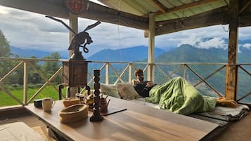 Una mesa de madera rústica con vistas a montañas, una persona relajándose y decoración tradicional.