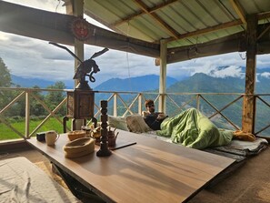 A rustic wooden table with a view of mountains, a person relaxing, and traditional decor.