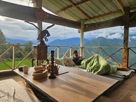 A rustic wooden table with a view of mountains, a person relaxing, and traditional decor.