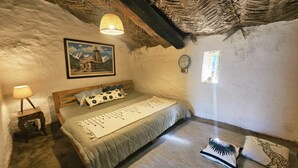 Un dormitorio con cama, mesita de noche, lámpara, un cuadro en la pared y una ventana.