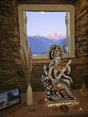 Una estatua de una deidad con múltiples brazos, un tocado decorativo y un telón de fondo de montañas.