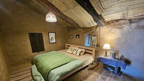 Una habitación rústica con una cama, una mesita con una lámpara y un estante en la pared.