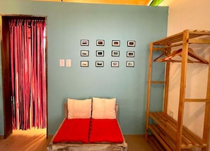 A room with a bed, a wooden wardrobe, and a wall with framed pictures.