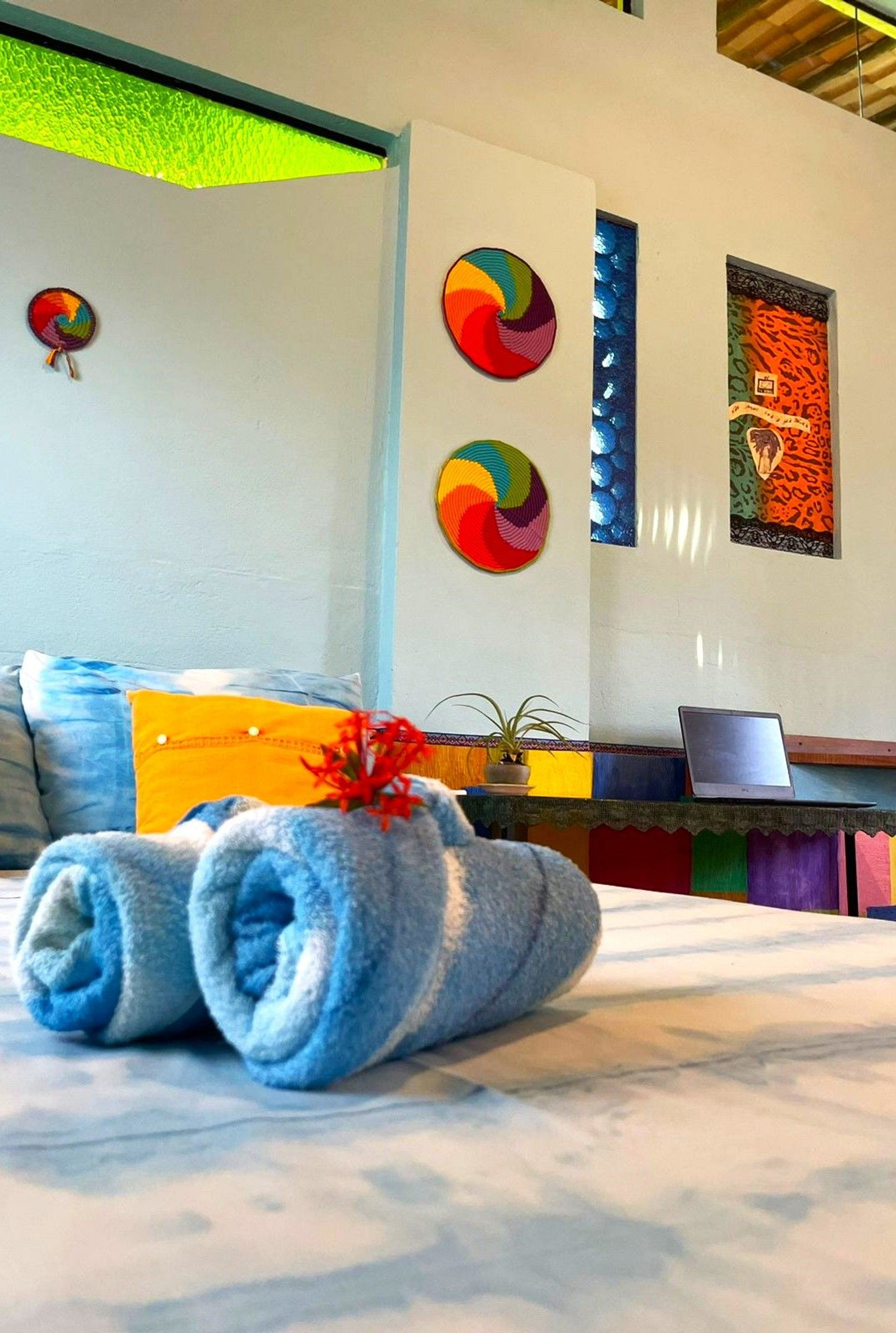 Quarto de hotel com cama, laptop sobre uma mesa e arte decorativa na parede.