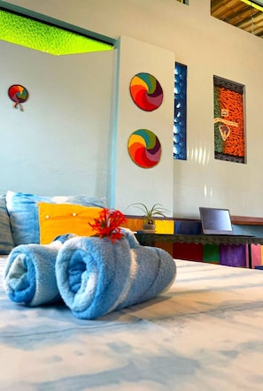 Quarto de hotel com cama, laptop sobre uma mesa e arte decorativa na parede.