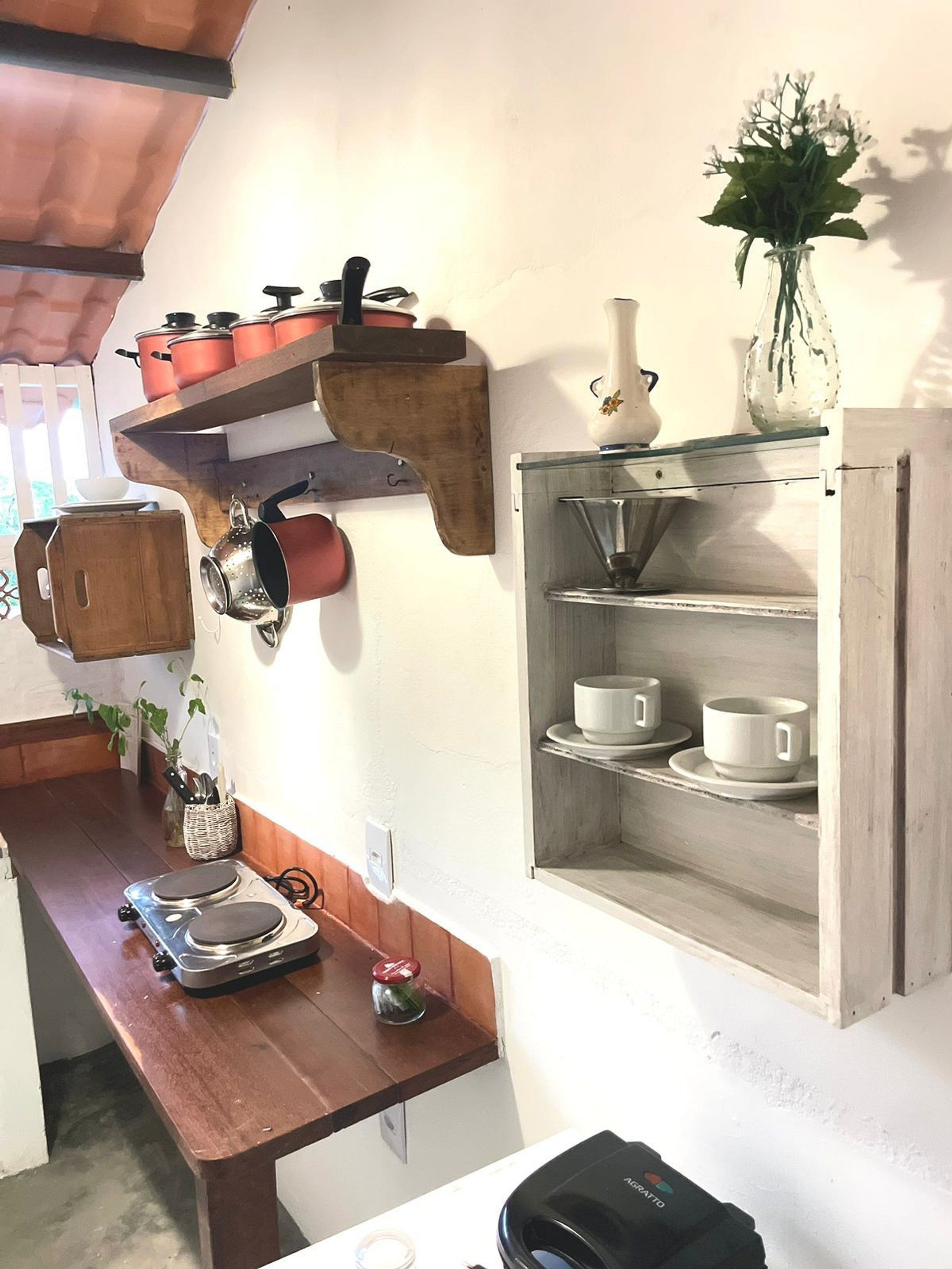 Une cuisine avec des étagères en bois où sont rangées des casseroles, une machine à café et un vase rempli de fleurs.