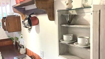 Una cocina con estantes de madera que sostienen ollas, una cafetera y un florero con flores.