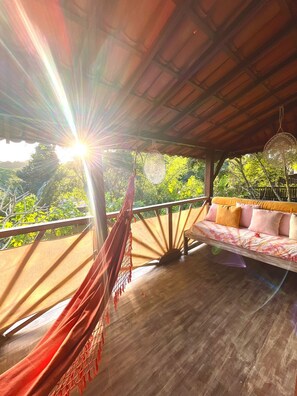 A hammock, a sofa, and a hanging light fixture in a covered outdoor area with a view of greenery. - MAR DÁ LIBERDADE com Vila Entreluas (Morro de São Paulo)