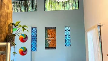 Una habitación con techo de madera, una lámpara colgante, pared colorida con obras de arte, una mesa con un ordenador portátil y una silla.