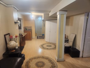 A spacious living area with a wooden floor, a dining table, a sofa, and a cabinet. There is a door leading to another room and a small kitchen area in the background. - Quiet Basement in Markham (Regional Municipality of York)